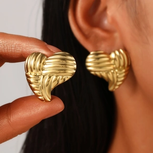 Detail of gold heart earrings with textured ribbed design shown on ear and held by hand