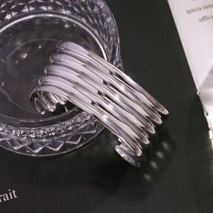 Detail of silver multi-layered wide open bangle draped over a glass on a green surface