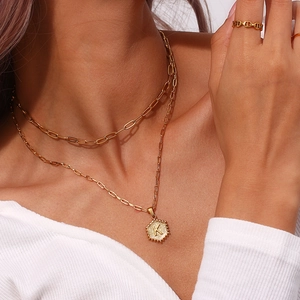 Detail of layered gold necklace with letter K pendant and hollow ring on model