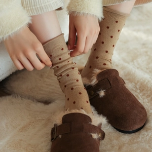 Close-up of beige polka dot wool socks paired with cozy brown suede slippers on a soft rug