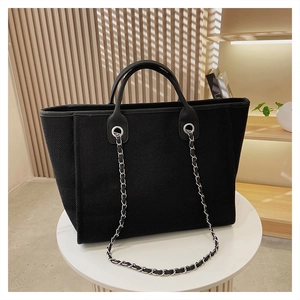 Detail of black canvas bucket tote bag featuring a metal chain handle on a display stand