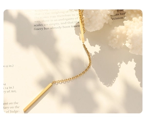 Detailed close-up of a 18K gold plated stainless steel long bar pendant on a book
