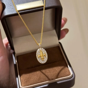Macro shot of 18k gold-plated oval pendant featuring fleur-de-lis and zircon inlays