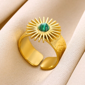 Adjustable gold sunburst ring with green turquoise stone on beige fabric background