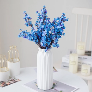 Blue artificial gypsophila flowers in a white textured ceramic vase on a desk