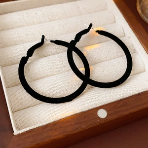 Detail view of black flocked hoop earrings presented in a wooden jewelry display box