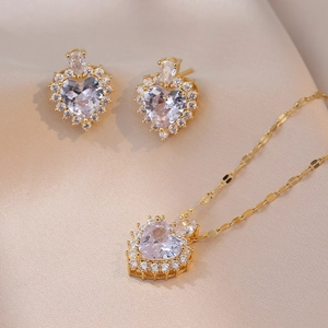 Detail of gold heart pendant necklace and stud earrings set with sparkling zircon stones