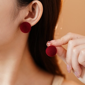 Close-up of red flocked round stud earrings worn by a model showing velvet texture