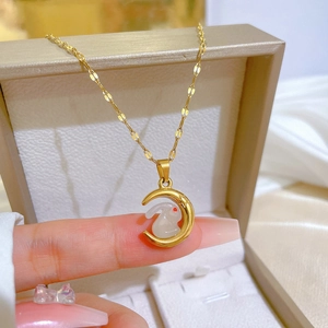 Minimalist gold moon and white jade rabbit pendant necklace held in hand over a gift box