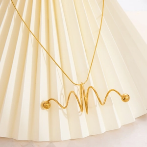 Collier double en or avec pendentif spirale et perles sur fond texturé de couleur crème