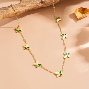 Elegante collana a farfalla dorata con gemme verdi esposta su un ramo di legno