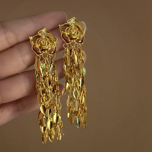 Détail des boucles d'oreilles longues rose dorée avec pompons élégants au fini métallique