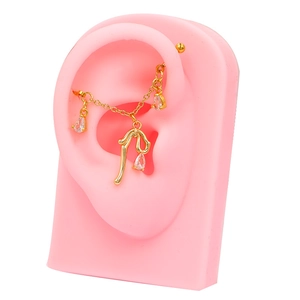 Close-up of golden industrial ear bar with chain and teardrop zircon charms on ear model