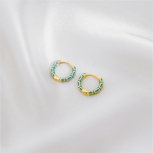 Detail view of gold hoop earrings with light blue geometric patterns on white silk fabric