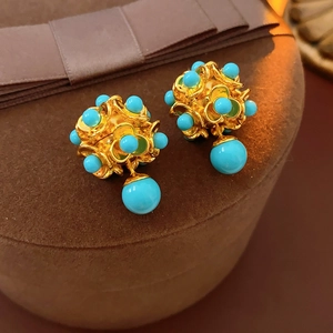 Détail de boucles d'oreilles fleur dorées avec perles turquoise sur un coffret