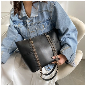 Detail of elegant black leather tote with gold metal chain strap on model's shoulder