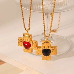 Detail of gold cross pendants with hammered texture and heart stones on twisted chains