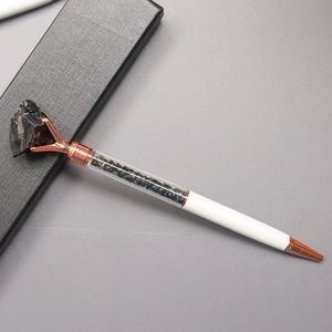 Detail of white metal ballpoint pen with rose gold trim and black crystal stone top