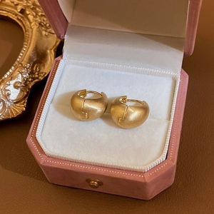 Details von matten goldenen Bohnen-Ohrringen auf einer zartrosa Schmuckschatulle