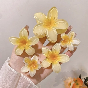 Hand holding set of five yellow frangipani flower hair claws in various sizes