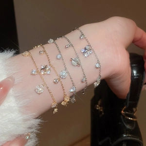 Detail of layered gold and silver zircon bracelets with Saturn and bow charms on wrist