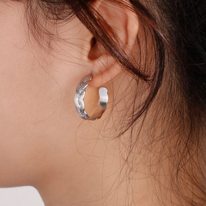 Detailed view of silver braided C-shape earrings on model showing textured metallic finish