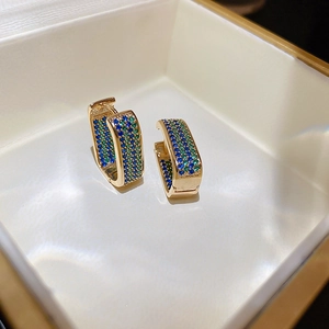 Macro detail of gold huggie earrings with pave-set blue and green geometric zircon crystals
