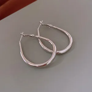 Minimalist silver oval drop hoop earrings with polished metal finish in close-up view