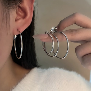 Set of minimalist silver hoop earrings in various sizes shown on ear and hand