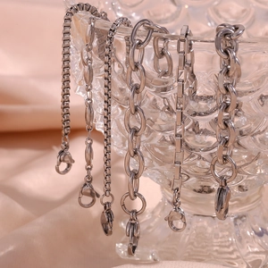 Detail of silver titanium steel anklets with lobster clasps on textured glass