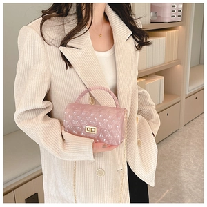 Pink jelly bag with quilted pattern and gold chain strap held by model in beige suit