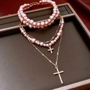 Pink pearl layered cross pendant necklace with rose gold chain on jewelry tray