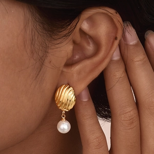 Elegant gold shell texture earrings with white round pearls shown on a female model