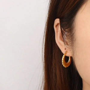 Close-up of golden croissant-style hoop earring on model with elegant spiral texture