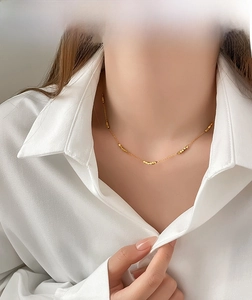 Detail view of a minimalist gold beaded necklace with square accents on a female model