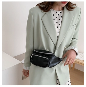 Fashionable black leather waist bag worn by model over a light green blazer jacket