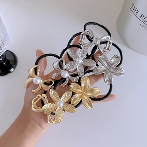 Close-up of golden and silver metal flower bow hair ties with pearls on black elastic