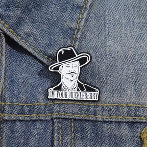Detail of I'M YOUR HUCKLEBERRY enamel pin featuring Doc Holliday on a denim jacket