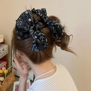 Détail d'une pince à cheveux avec nœud en tissu imprimé paisley noir portée par un mannequin