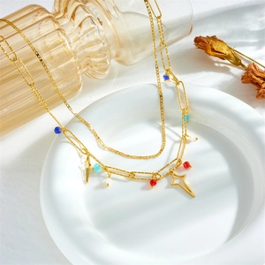 Detail of gold layered chain necklace with colorful beads and cross pendants on white plate