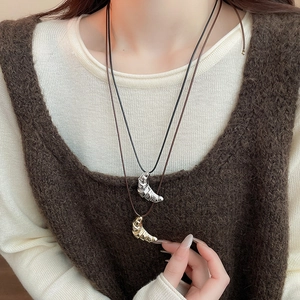 Detail shot of a creative croissant pendant necklace worn with a knit sweater for styling