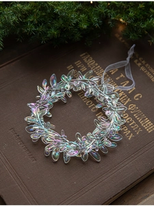 Iridescent acrylic leaf wreath Christmas ornament with ribbon on vintage book background