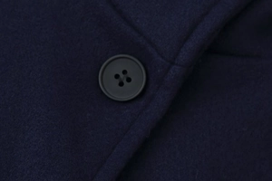 Detail of navy blue wool coat fabric with a matte four-hole resin button and clean stitching