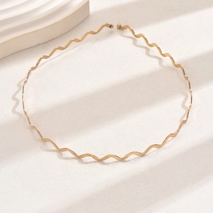 Detailed top view of a minimalist golden wavy metal headband on a beige textured surface