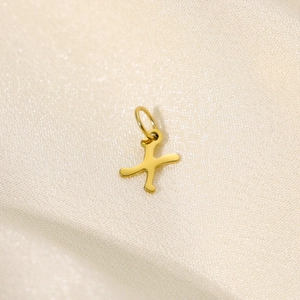 Detailaufnahme eines goldenen Edelstahl-Buchstaben-X-Anhängers auf weichem Seidenstoff