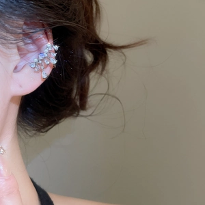 Detailed close-up of a silver bow ear cuff with zircons and pearls on a model's ear