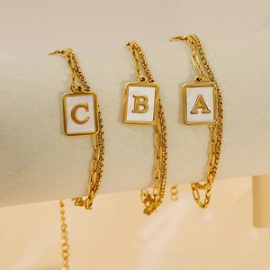Détail de bracelets en chaîne dorée avec pendentifs alphabet A B C sur incrustation nacre