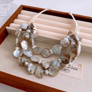Bohemian triple-layer shell bead necklace with iridescent stones on a brown velvet pad