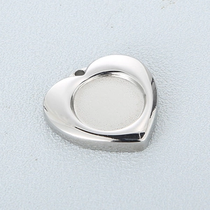 Polished silver heart pendant with circular indentation and metal luster on gray surface