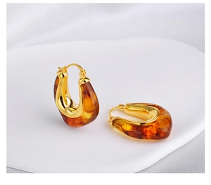 Macro shot of U-shaped amber resin earrings with polished gold metal finish